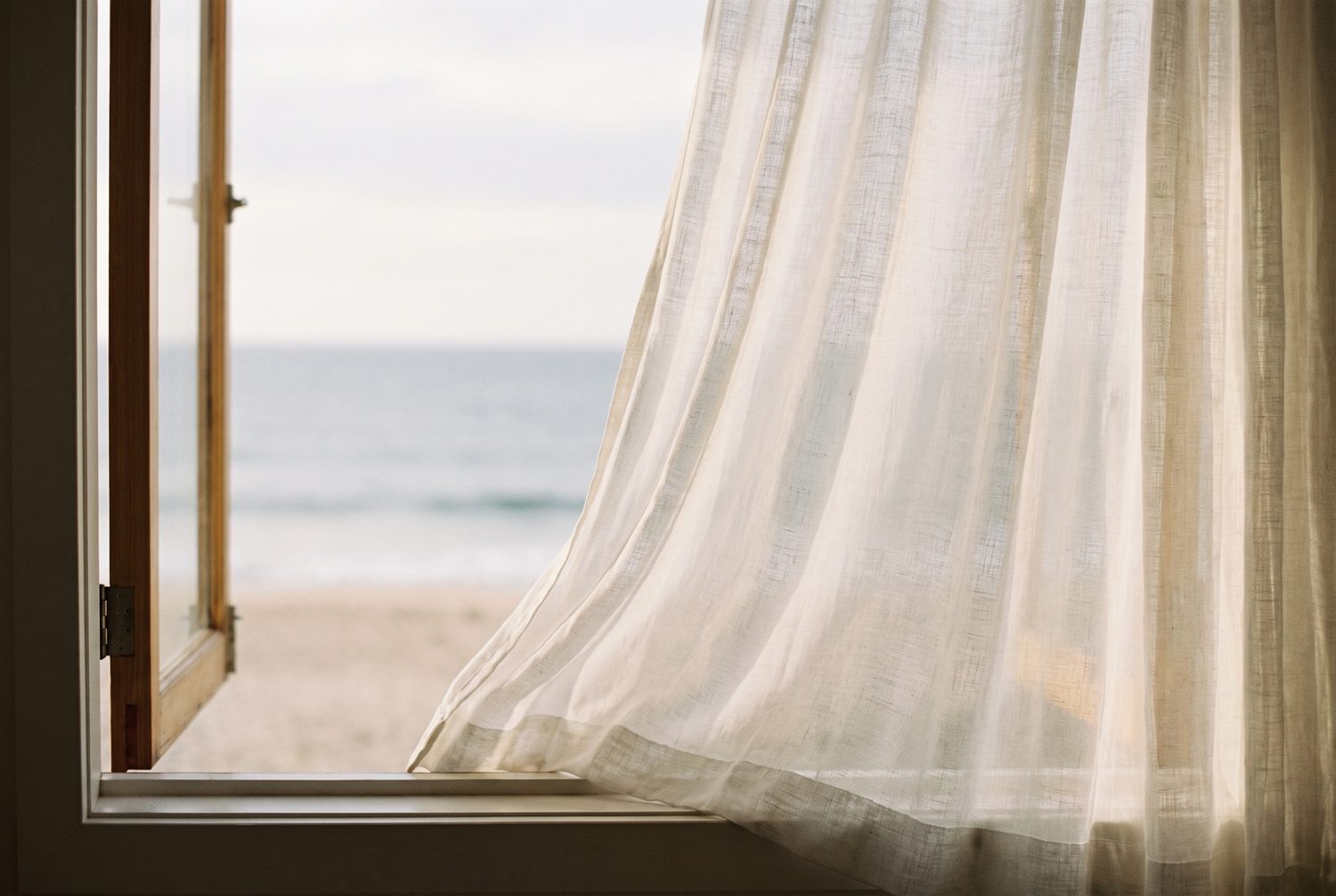 Sheer curtain drifting in the sea breeze by an open window with an ocean view